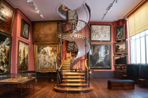 Escalier en colimaçon majestueux au cœur d'un musée insolite à Paris, entouré de tableaux sombres et évocateurs.