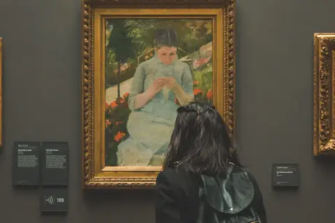 Une visite au musée gratuit premier dimanche du mois. Une jeune femme admire un tableau représentant une jeune fille tricotant dans un jardin.