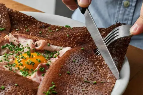Une galette complète, garnie d'œuf, jambon et ciboulette. Une bouchée des meilleures crêpes à Paris.