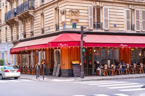 Un café parisien avec des tables en terrasse sous un auvent rouge. L'ambiance d'un food court à Paris.