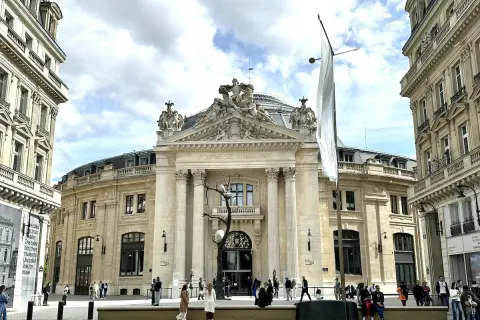 Le musée de la Bourse, un bâtiment majestueux, accueille des visiteurs sous un ciel nuageux. Une sculpture d'arbre intrigante se dresse devant l'entrée.