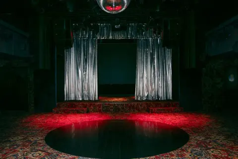Scène de concert avec rideaux argentés, tapis persan et boule disco rougeoyante, évoquant l'ambiance d'un bus palladium.