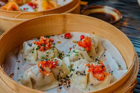 Délicieux dim sum à Paris, servis dans un panier en bambou, garnis de garnitures vibrantes et de graines de sésame.