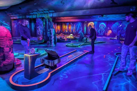Ambiance sous-marine pour un escape game avec enfant. Parcours de mini-golf fluorescent, décoré de méduses et de dauphins, promettant une aventure ludique.
