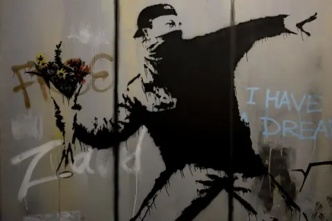 Un homme lance des fleurs, un message d'espoir du musée Banksy Paris. "I have a dream" écrit en bleu.