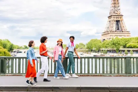Quatre amis profitent d'une visite insolite Paris gratuit, traversant un pont avec la Tour Eiffel en arrière-plan.