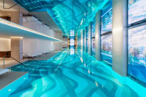 Piscine intérieure luxueuse d'un spa à Paris, avec un éclairage bleu vif, des voilages blancs et une vue sur la ville.