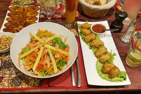 Un festin dans un restaurant antillais : salade de crevettes, accras, bananes plantain frites et un cocktail rafraîchissant.
