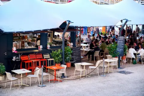 Bar animé sur les quais parisiens, avec des tables et des chaises en terrasse sous une grande tente blanche.