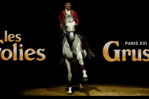 Une écuyère en tenue rouge sublime un cheval blanc lors d'un spectacle des Folies Gruss.