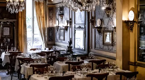 Tables dressées dans le plus vieux restaurant de Paris. Lustres en cristal, papier peint orné et vue sur la rue.