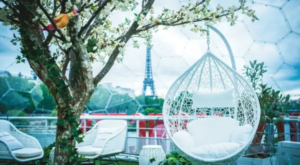Un décor romantique pour un speed dating Paris, avec la Tour Eiffel en arrière-plan. Fauteuils blancs, balancelle et arbre fleuri créent une ambiance féerique.
