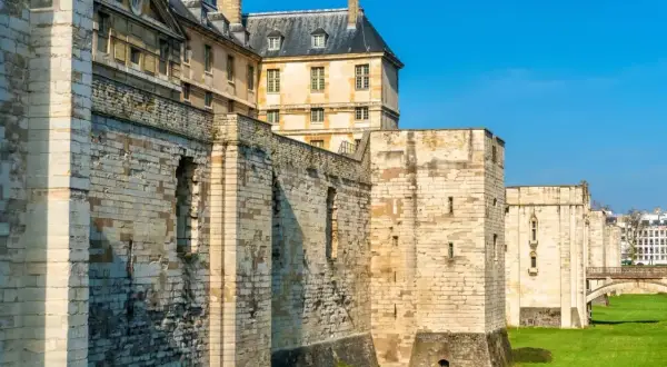 Murs imposants et tours de pierre du **château de Vincennes** sous un ciel bleu éclatant, avec des bâtiments historiques en arrière-plan.