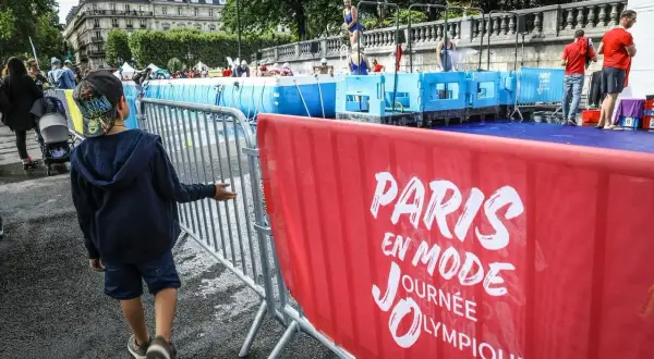 Un enfant observe une piscine temporaire installée pour une journée olympique à Paris. L'inscription "Paris en mode Journée Olympique" est visible sur une banderole rouge.