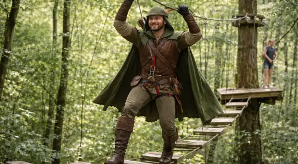 Un homme en costume de Robin des Bois traverse un pont suspendu dans un parc d'accrobranche, une aventure à Paris.