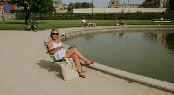Une femme lit au soleil, profitant d'un moment de détente pour ou bronzer à Paris, près d'un bassin.