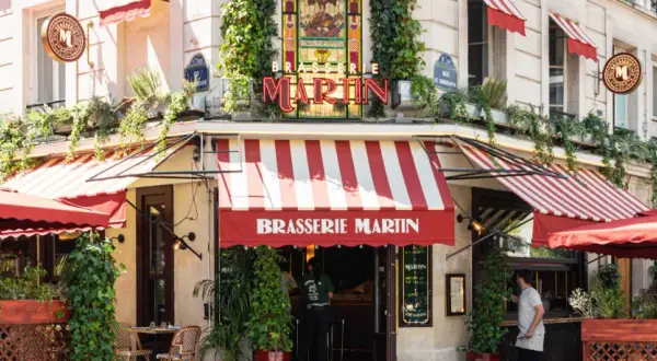La Brasserie Martin, un coin parisien charmant avec ses auvents rayés rouges et blancs, ses plantes grimpantes et son enseigne lumineuse.