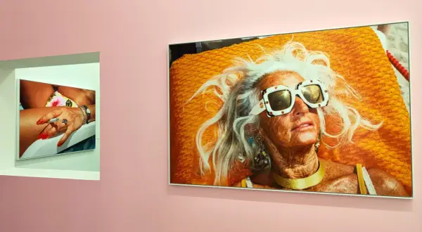 Une femme âgée aux cheveux blancs et lunettes de soleil extravagantes, sur une serviette orange vif. Une autre photo montre une main manucurée tenant une cigarette. Martin Parr expo.