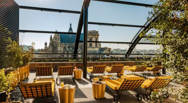 Profitez d'un brunch rooftop à Paris avec vue sur les toits et une église majestueuse. Des chaises longues jaunes invitent à la détente.