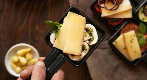 Poignée de raclette avec fromage, champignons et basilic, prêt pour un dîner dans un restaurant raclette Paris.