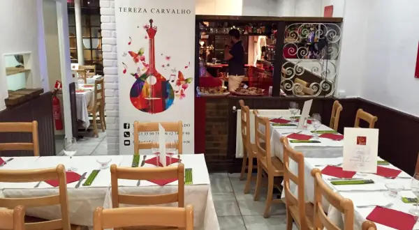 Tables dressées dans un restaurant portugais. Un homme derrière le bar, une guitare colorée sur une bannière.