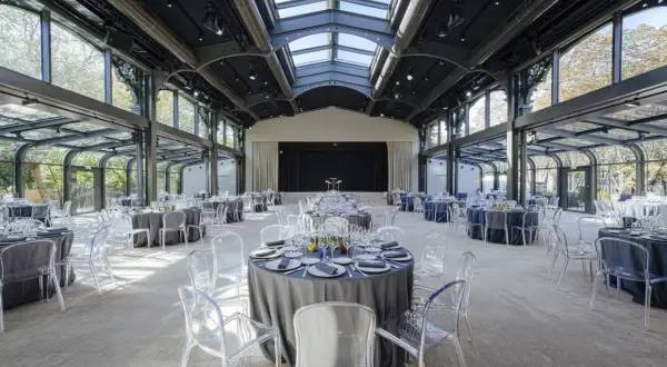 Salle de réception lumineuse au pavillon Gabriel, tables rondes dressées sous une verrière, chaises transparentes.