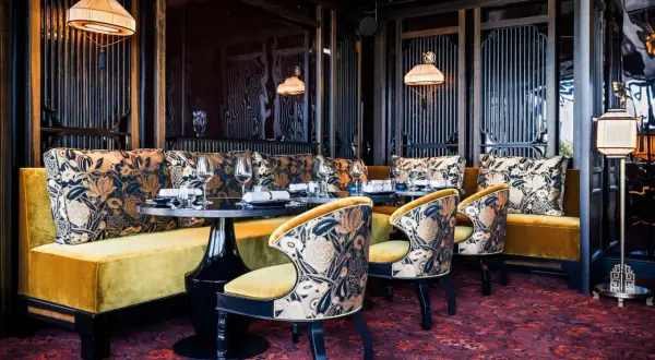 Ambiance luxueuse d'un restaurant à mun paris. Banquettes velours ocre, coussins fleuris, chaises élégantes et tapis persan.