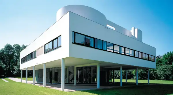 La Villa Savoye, icône de l'architecture moderne, se dresse sur pilotis dans un écrin de verdure, sous un ciel bleu éclatant.