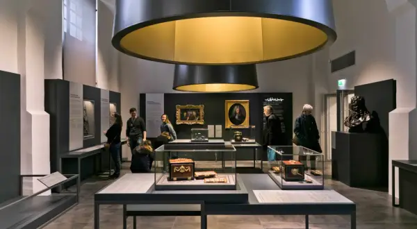 Visiteurs admirant des objets d'art et des portraits dans une exposition au musée Monnaie de Paris.