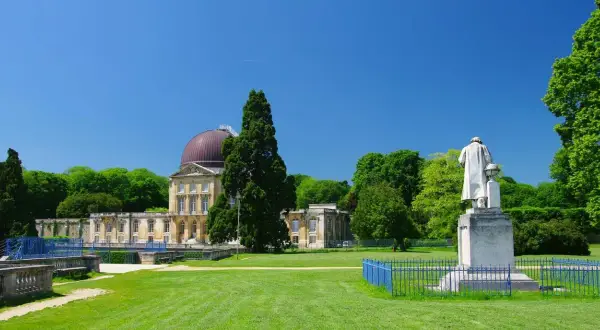 Un grand bâtiment avec un dôme rouge, entouré d'arbres verts et d'une pelouse. Une statue se dresse devant, comme si elle surveillait le hangar Y.
