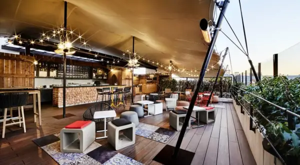 Ambiance chaleureuse sur un rooftop Paris pas cher, avec bar en bois, lumières scintillantes et mobilier cosy. Idéal pour un moment détente.