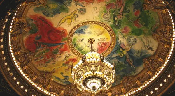 Le plafond peint de la **place de l'Opéra** est illuminé par un lustre doré. Des figures célestes dansent sur une toile colorée.