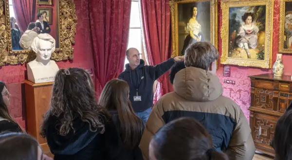 Visite guidée dans la Maison de Victor Hugo à Paris. Un guide montre des tableaux et un buste de l'écrivain à un groupe de visiteurs.