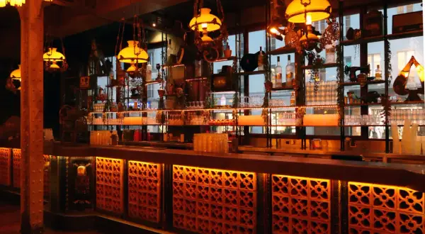 Ambiance chaleureuse d'un bar parisien, avec des lumières tamisées, des étagères remplies de bouteilles et de bibelots, évoquant un **barrio latino** à Paris.