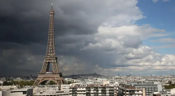 La Tour Eiffel, une des célèbres structures conçues par Gustave Eiffel, se dresse fièrement au-dessus de Paris sous un ciel orageux et lumineux.