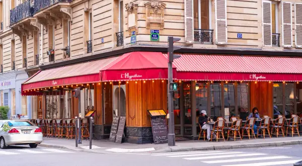 Un café parisien avec des tables en terrasse sous un auvent rouge. L'ambiance d'un food court à Paris.
