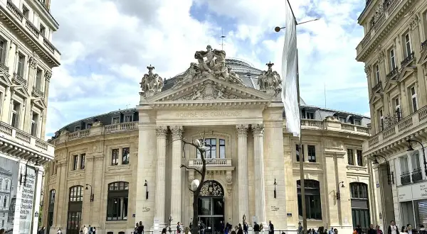 Le musée de la Bourse, un bâtiment majestueux, accueille des visiteurs sous un ciel nuageux. Une sculpture d'arbre intrigante se dresse devant l'entrée.