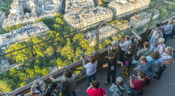 Vue panoramique de Paris depuis la Tour Eiffel, avec des touristes admirant le paysage. Le soleil d'été suggère le meilleur moment pour visiter la Tour Eiffel.