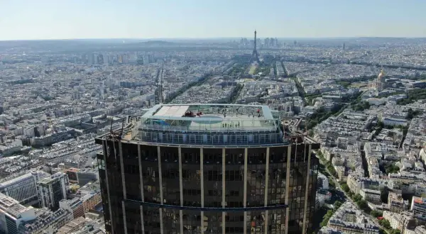 Vue aérienne de la **Tour Montparnasse** avec sa terrasse panoramique. Paris s'étend à perte de vue, avec la Tour Eiffel au loin.