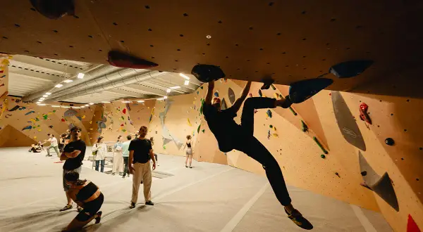 Grimpeurs s'entraînant à l'arkose de Strasbourg Saint-Denis, un mur d'escalade intérieur avec des prises colorées.