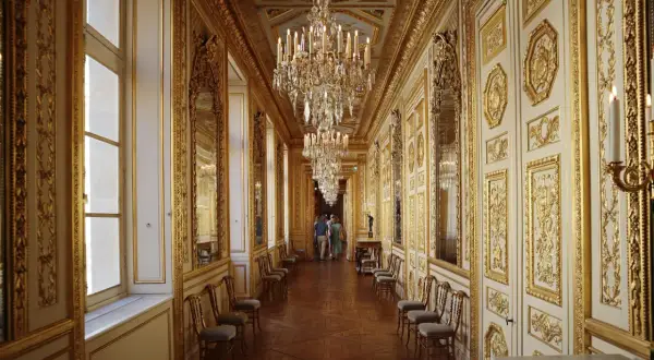 Un long couloir orné de dorures et de lustres étincelants, rappelant la splendeur du **hôtel de la Marine**.