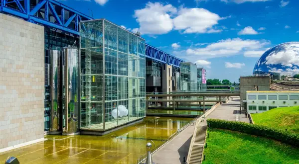 Le bâtiment moderne de la Cité des sciences Paris, avec ses structures en verre et en métal, reflète le ciel bleu et les nuages.