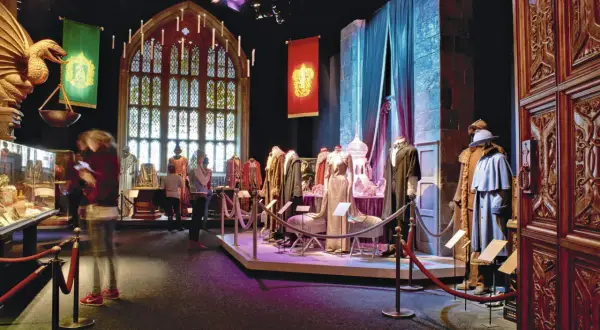 Costumes et artefacts de l'exposition Harry Potter, avec des bannières de Poudlard et une grande fenêtre gothique.