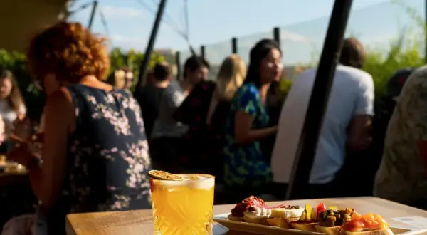 Cocktail et tapas sur une terrasse de toit à Paris, avec des gens en arrière-plan.
