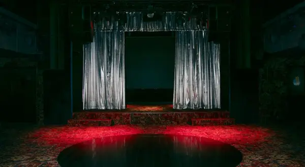 Scène de concert avec rideaux argentés, tapis persan et boule disco rougeoyante, évoquant l'ambiance d'un bus palladium.