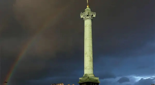 La colonne de Juillet se dresse fièrement sur la place de la Bastille, sous un ciel orageux traversé par un arc-en-ciel.