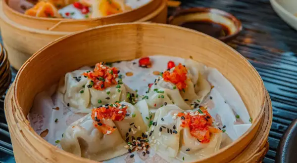 Délicieux dim sum à Paris, servis dans un panier en bambou, garnis de garnitures vibrantes et de graines de sésame.