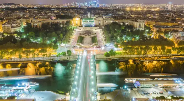 Paris la nuit, le scintillement de la Tour Eiffel se reflète sur la Seine, illuminant la ville.