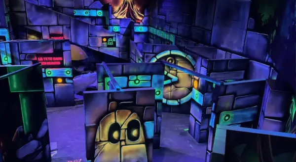 Labyrinthe de laser game aux couleurs vives, avec des fantômes et un volcan en arrière-plan. Le panneau "LA TÊTE DANS LES NUAGES" suggère une expérience amusante.