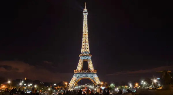 La Tour Eiffel illuminée la nuit, un spectacle magique avec des faisceaux de lumière traversant le ciel parisien.